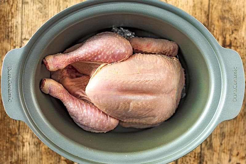 A slow cooker pot with a whole chicken in it.