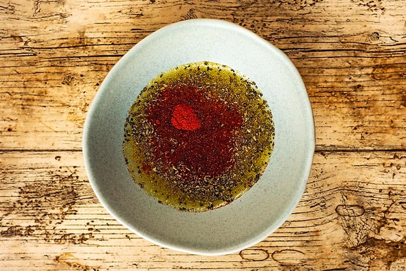 A small bowl with an oil and herb dressing in it.