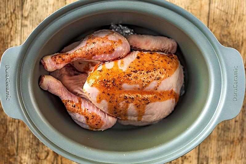 A slow cooker pot with a whole chicken covered in a sauce.
