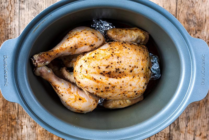 A cooked whole chicken in a slow cooker pot.