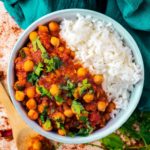 Moroccan Chickpea Stew in a bowl with rice surrounded by spices and chopped cilantro.