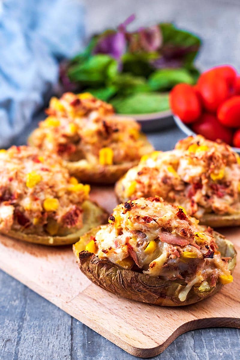 Four stuffed baked potatoes on a serving board.