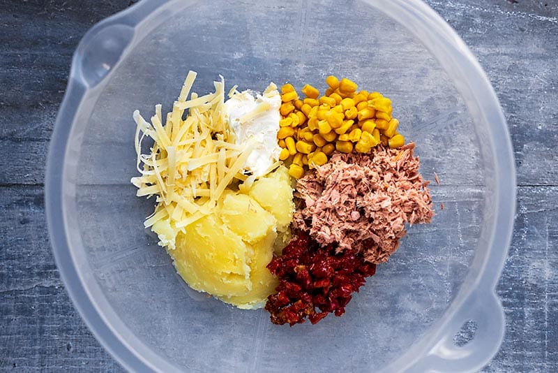 A mixing bowl containing cooked potato, cheese, sweetcorn, tuna and tomatoes.