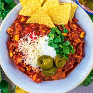 Turkey Chilli in a white bowl topped with tortilla chips and jalapenos.