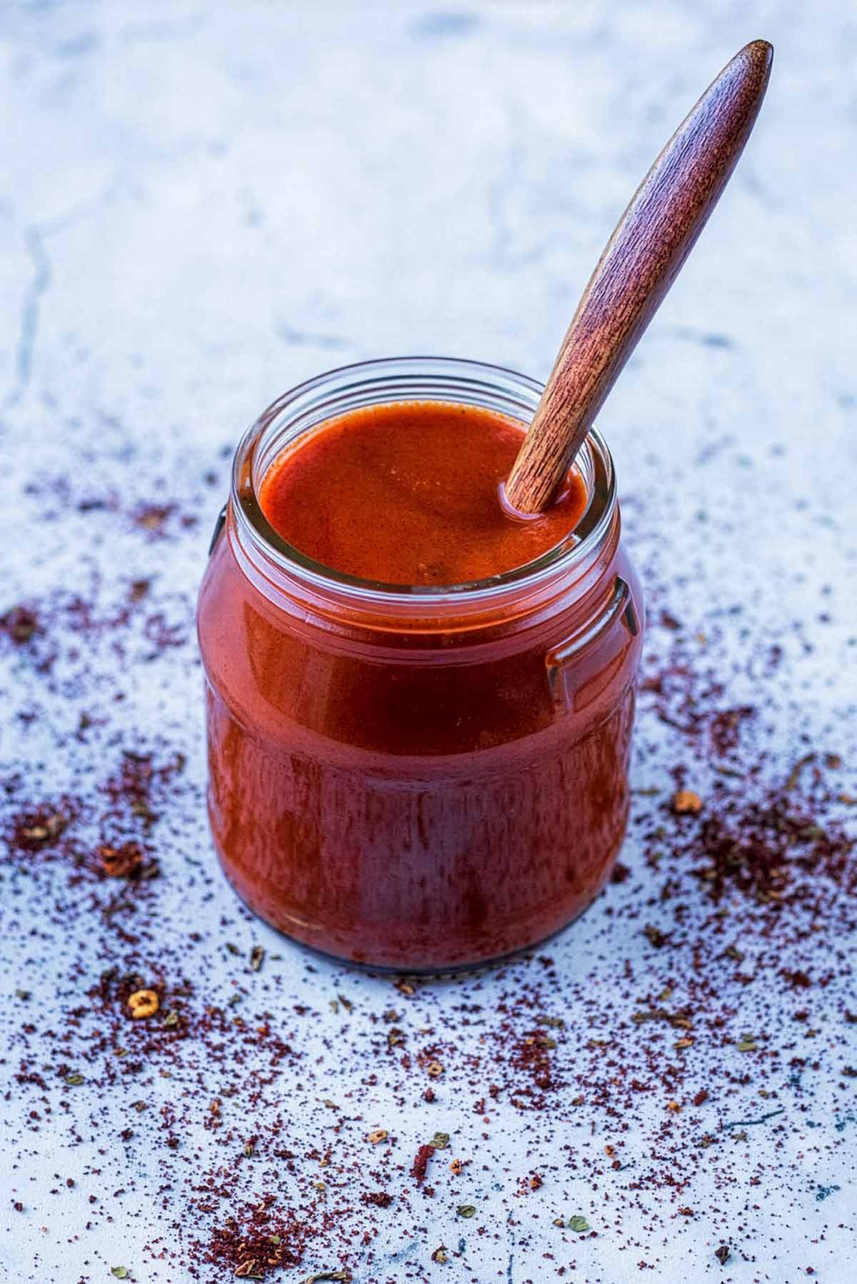 Enchilada sauce in a jar with a small wooden spoon.