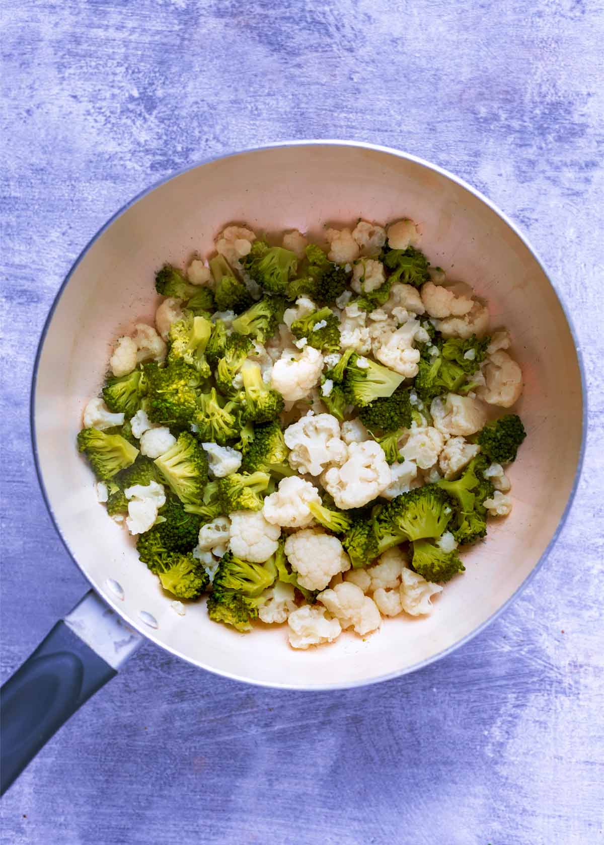 A saucepan containing small florets of broccoli and cauliflower.