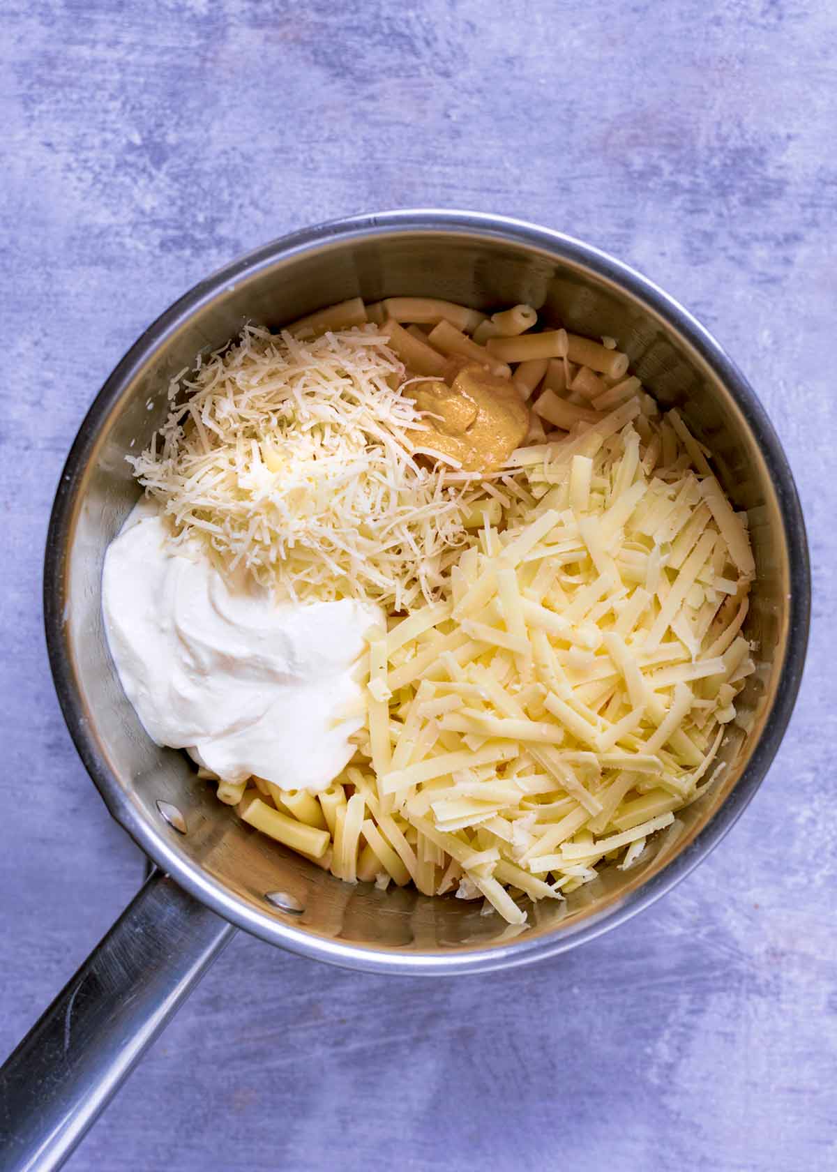 A saucepan containing macaroni, grated cheese, cream and mustard.