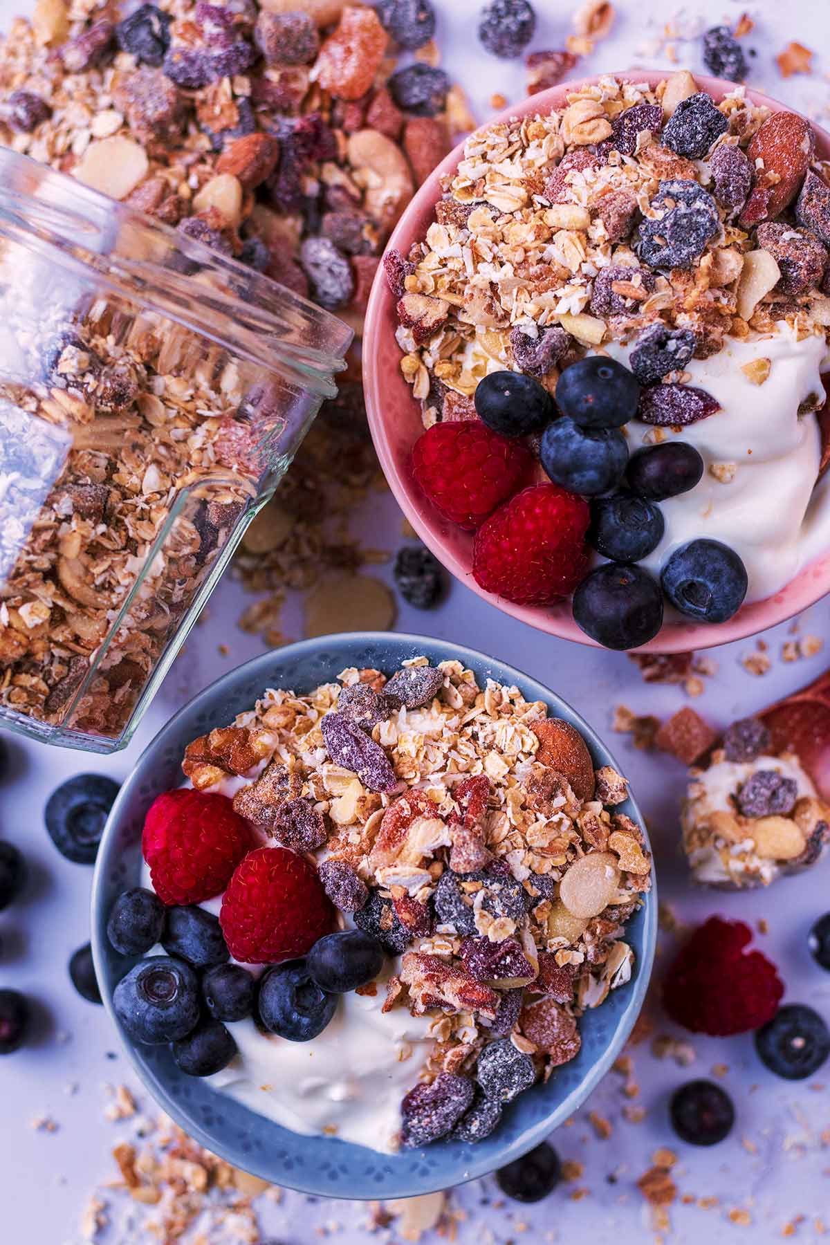 Two bowls of yogurt topped with muesli and berries.