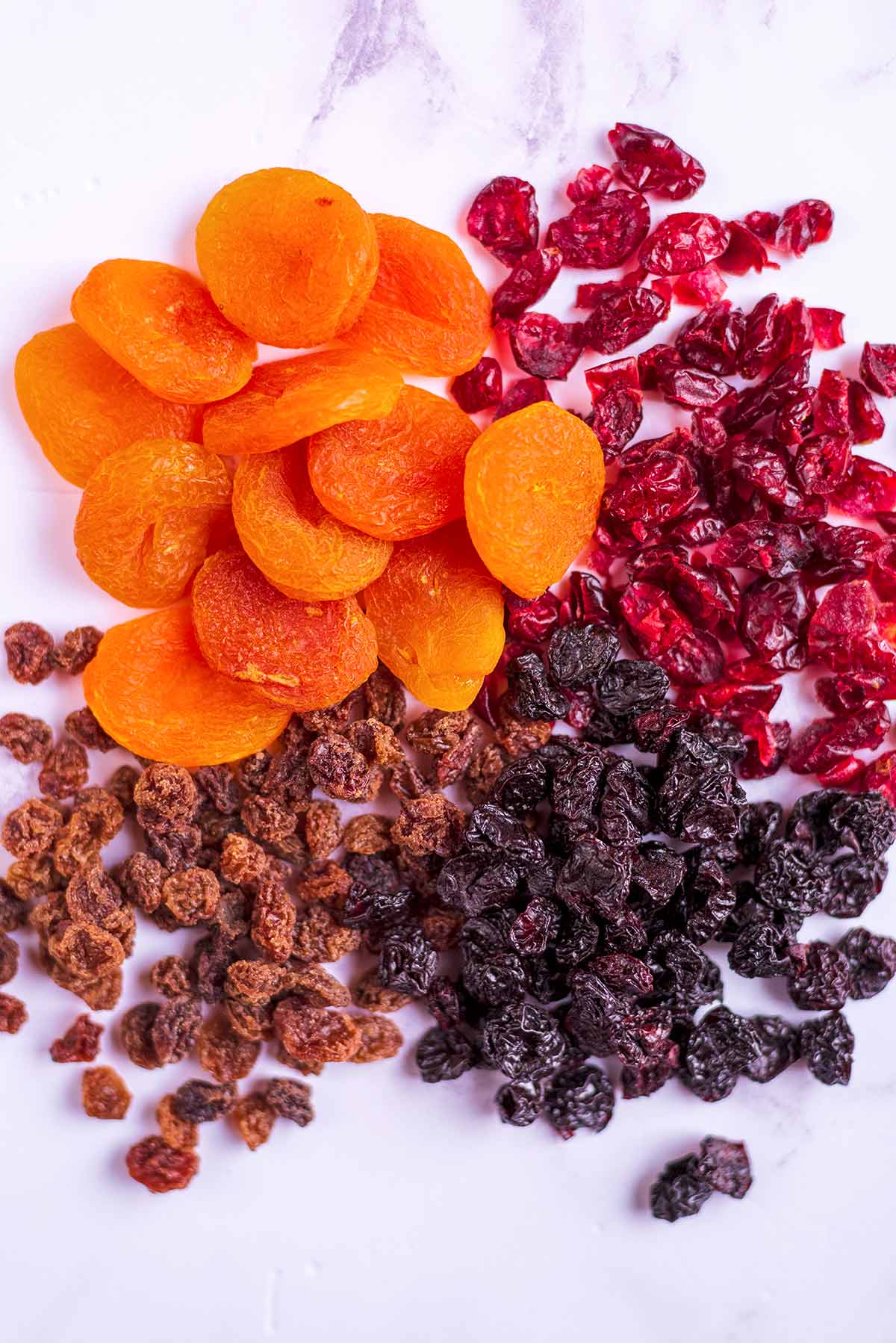 Dried apricots, cranberries, raisins and sultanas on a marble surface.
