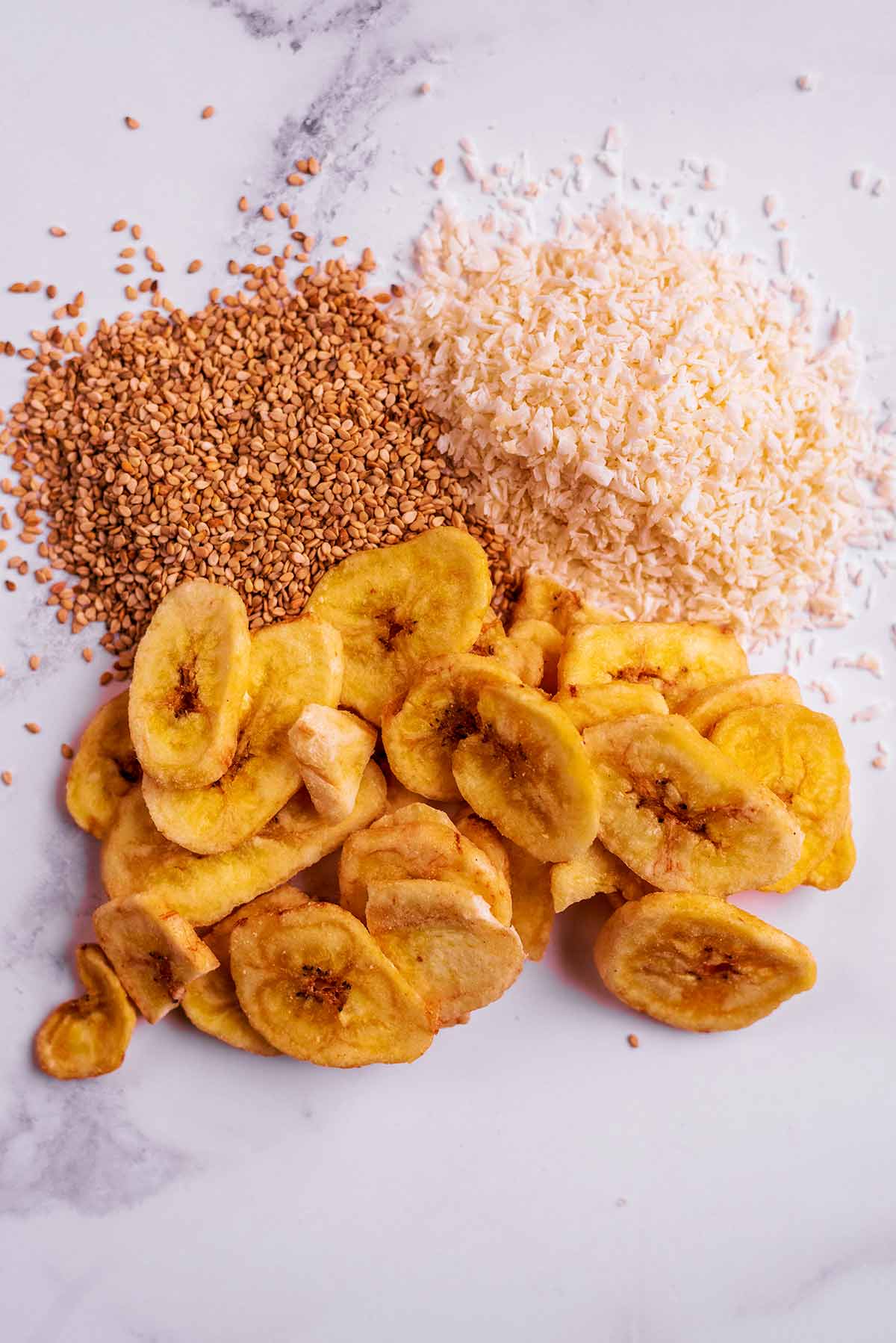Dried banana slices, desiccated coconut and flax seeds on a marble surface.