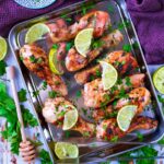 Honey Lime Chicken on a baking sheet topped with herbs and lime slices.