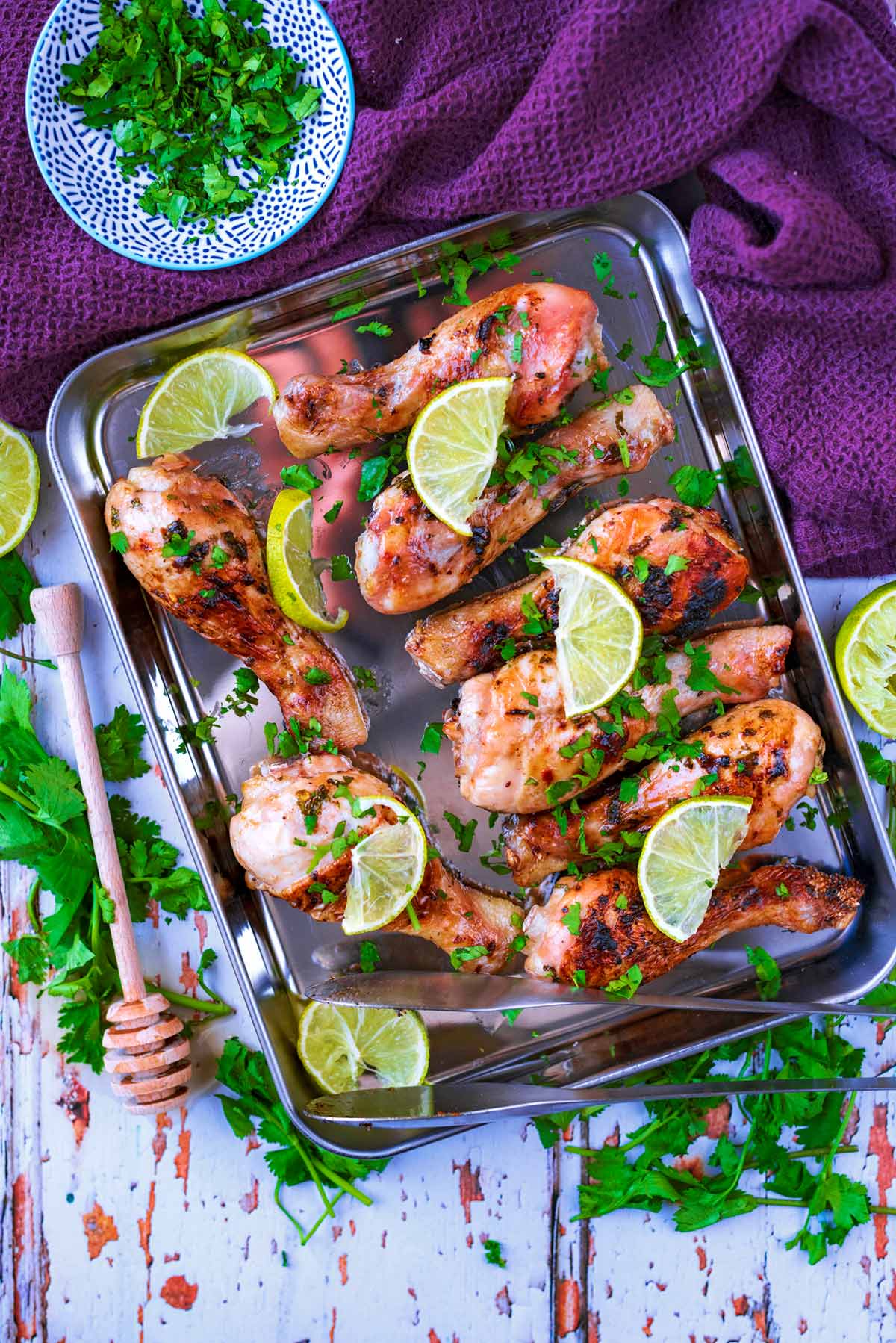 Eight cooked chicken drumsticks on a baking sheet with lime slices on them.