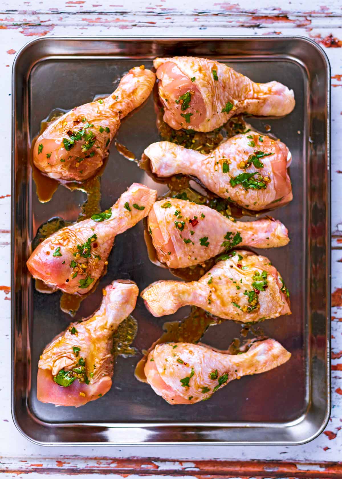 Eight marinated chicken drumsticks on a baking tray.