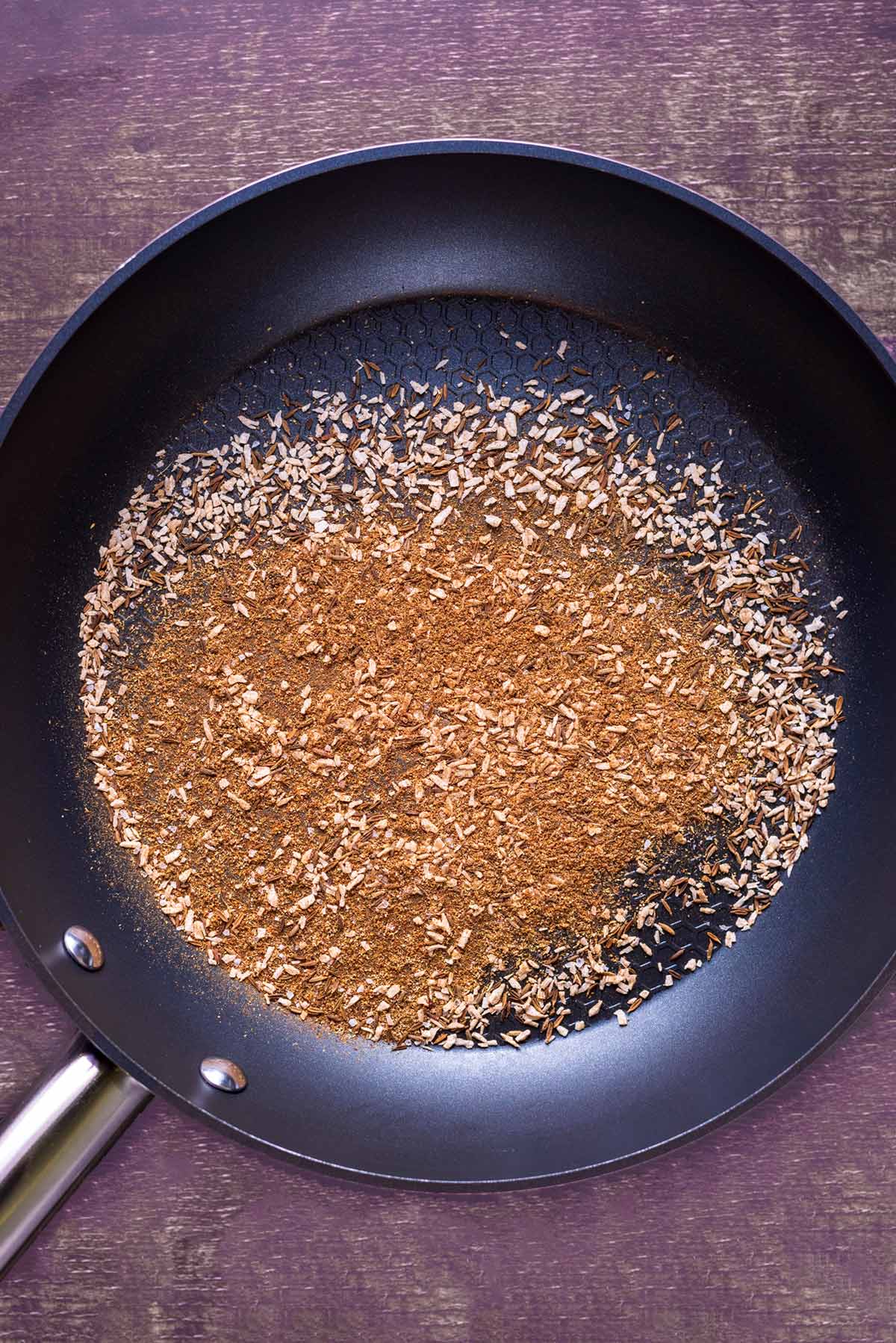 A frying pan with a mixture of spices toasting in it.