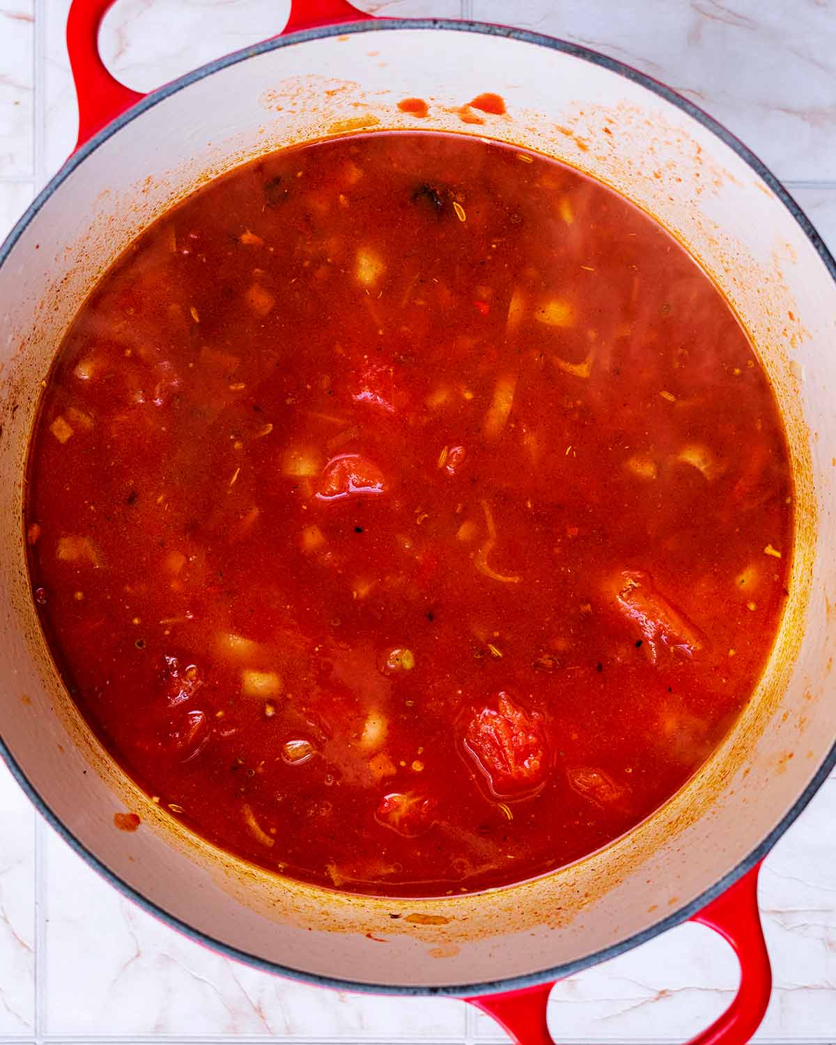 A large pan with a tomato sauce cooking in it.