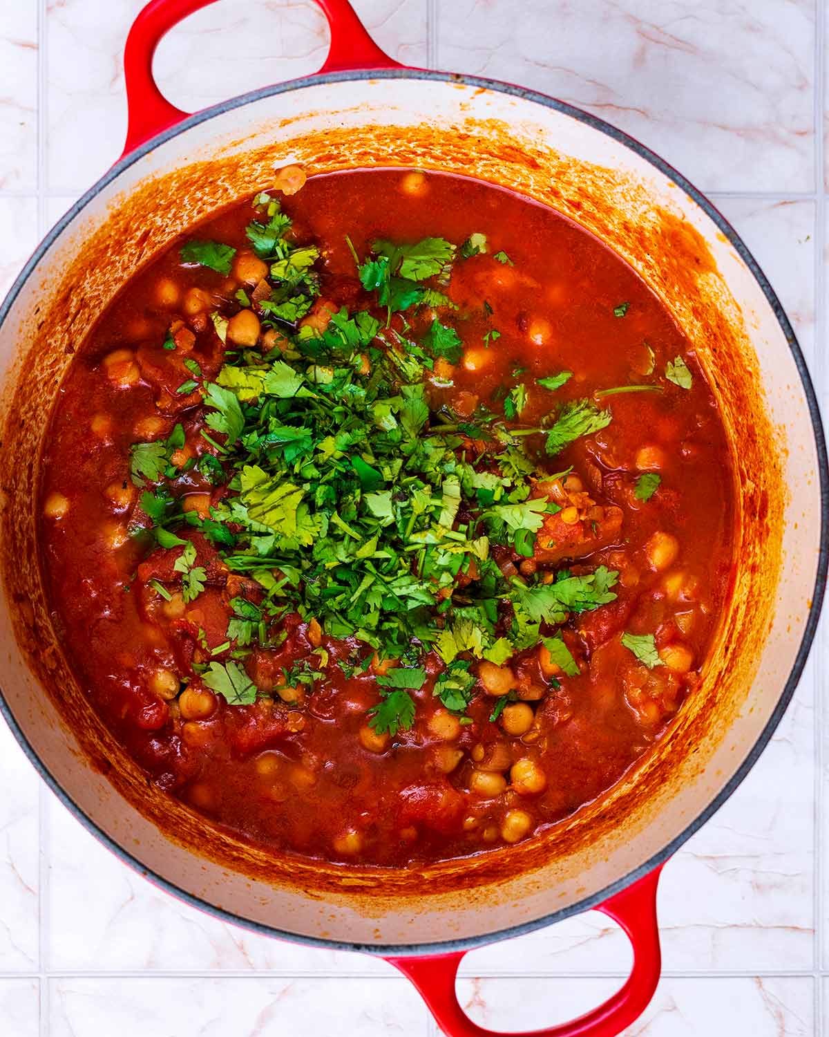 Chickpeas cooing in a tomato sauce with a large pile of chopped coriander on top.
