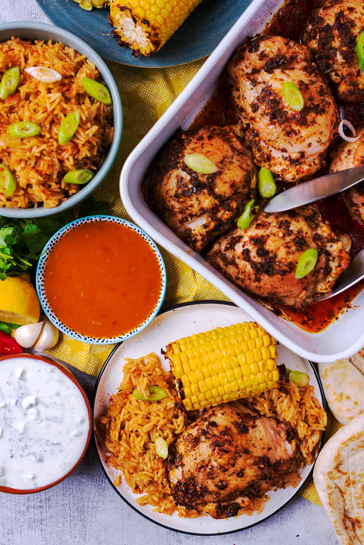 Peri Peri Chicken in a baking dish and on a plate with corn, rice, sauces and bread.