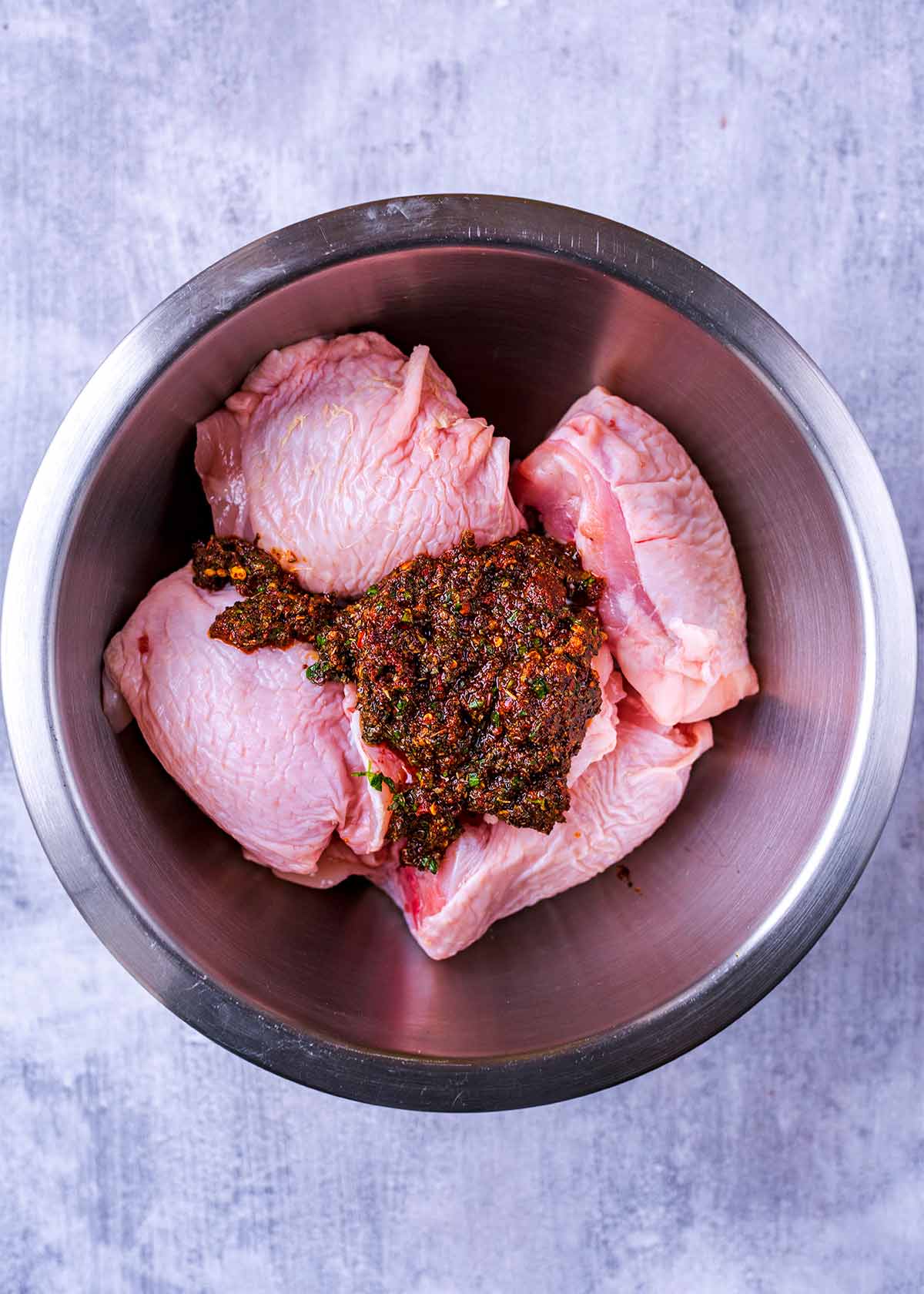 Raw chicken thighs in a mixing bowl with the marinade.