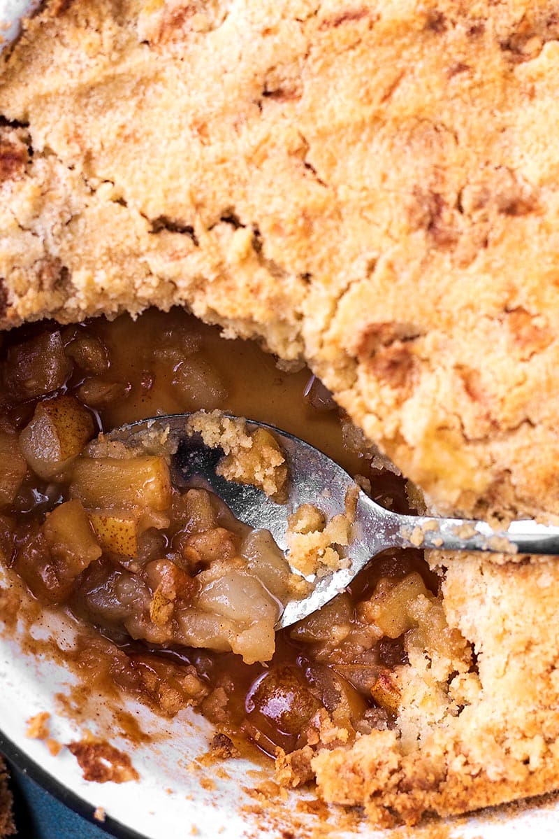 A crumble in a baking dish with a spoon in a scooped out area.