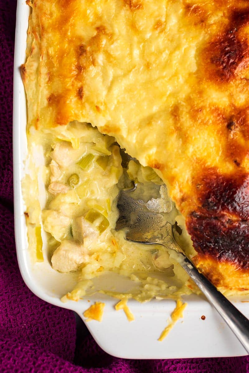 A baking dish containing chicken and leek pie with a corner scooped out.