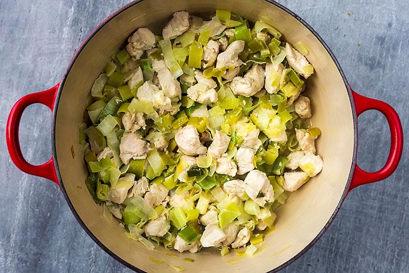 A large pan with chunks of chicken and sliced leeks cooking in it.
