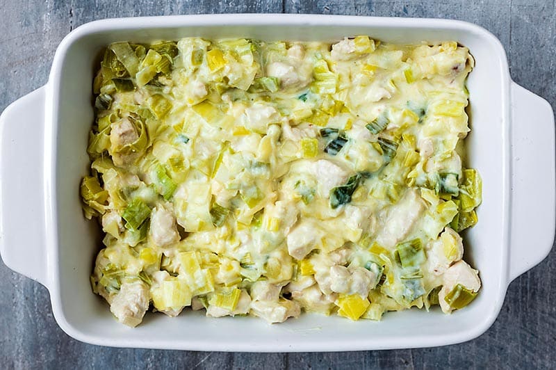 A baking dish with a creamy chicken and leek mixture at the bottom.