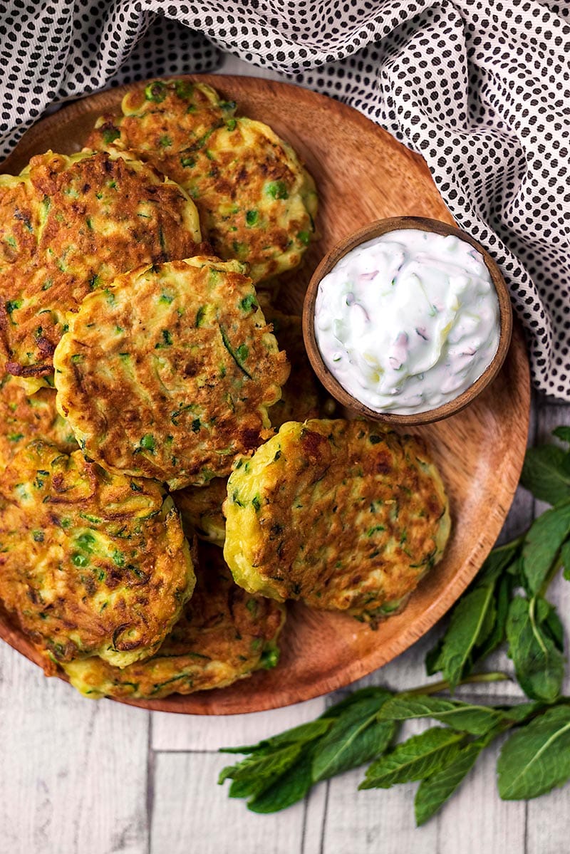 A plate of courgette fritters with a small dish of creamy tzatziki.