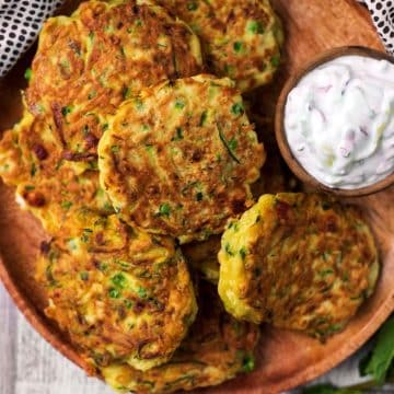 Easy Courgette Fritters on a wooden plate with a bowl of tzatziki
