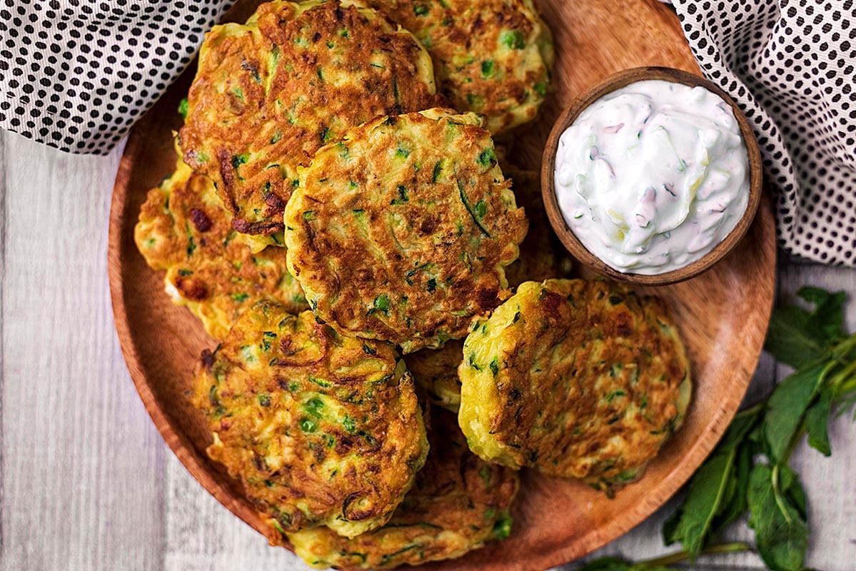 Easy Courgette Fritters on a wooden plate with a bowl of tzatziki.
