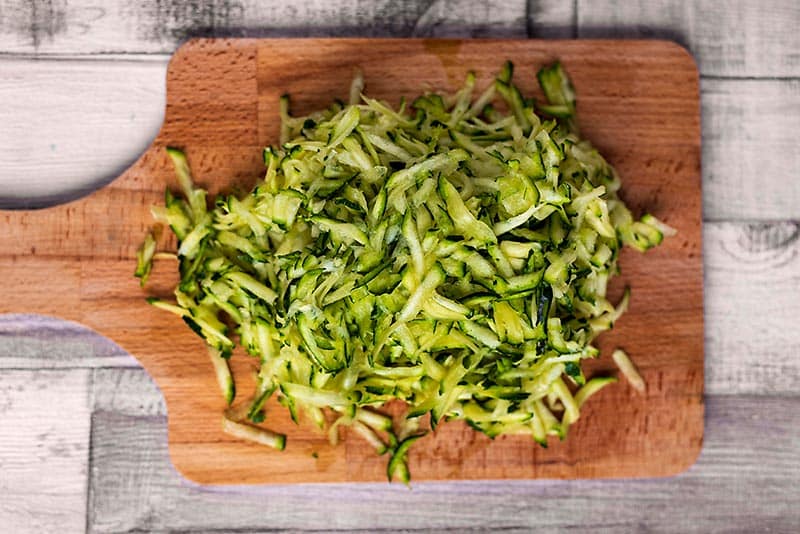 A chopping board with a pile of grated zucchini on it.