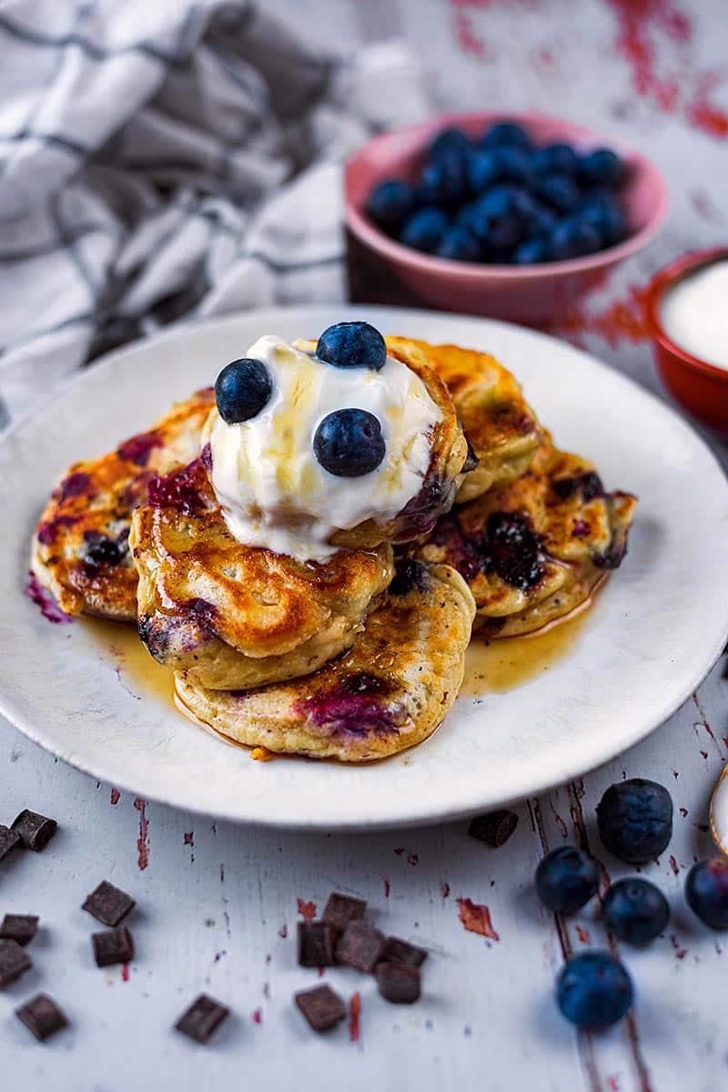A plate of pancakes in front of a bowl of blueberries.