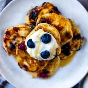 A plate of easy mini pancakes topped with a dollop of yogurt and some blueberries
