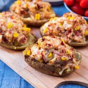 Four stuffed baked potatoes on a wooden serving board