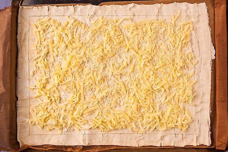 A sheet of pastry with grated cheese covering it