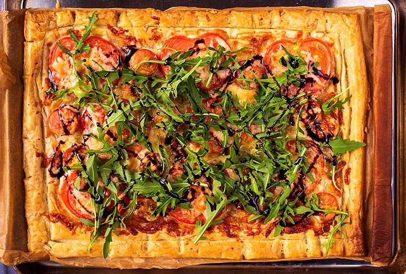 Tomato tart topped with arugula and a drizzle of balsamic