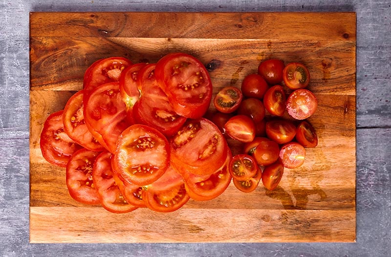 A wooden chopping board with various sliced tomatoes on it