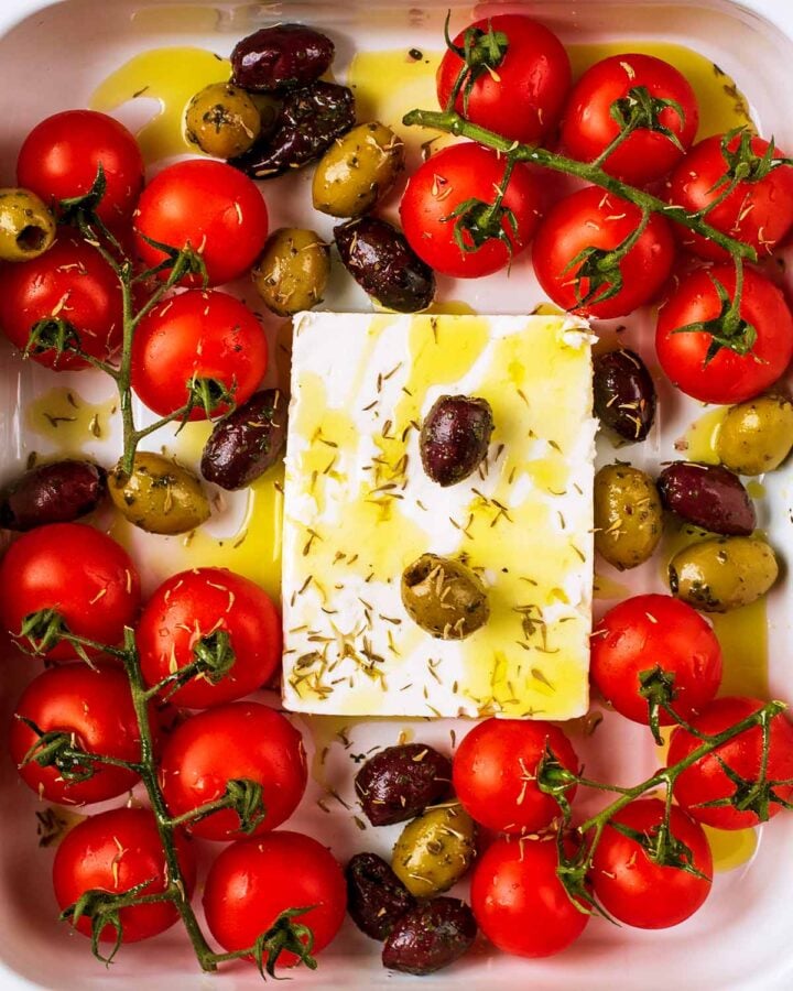 Feta, tomatoes and olives in a baking dish. Oil has been drizzled over everything.
