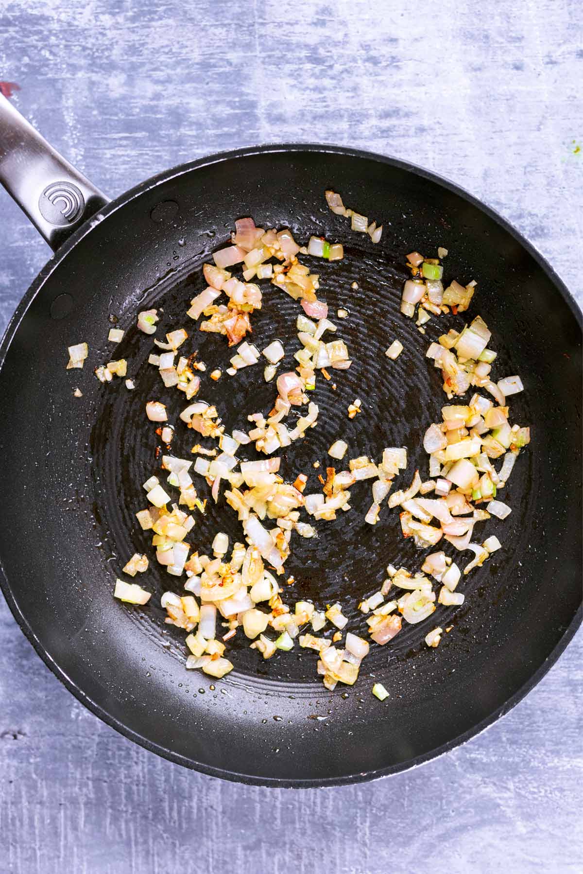 A frying pan with chopped onions cooking in it.