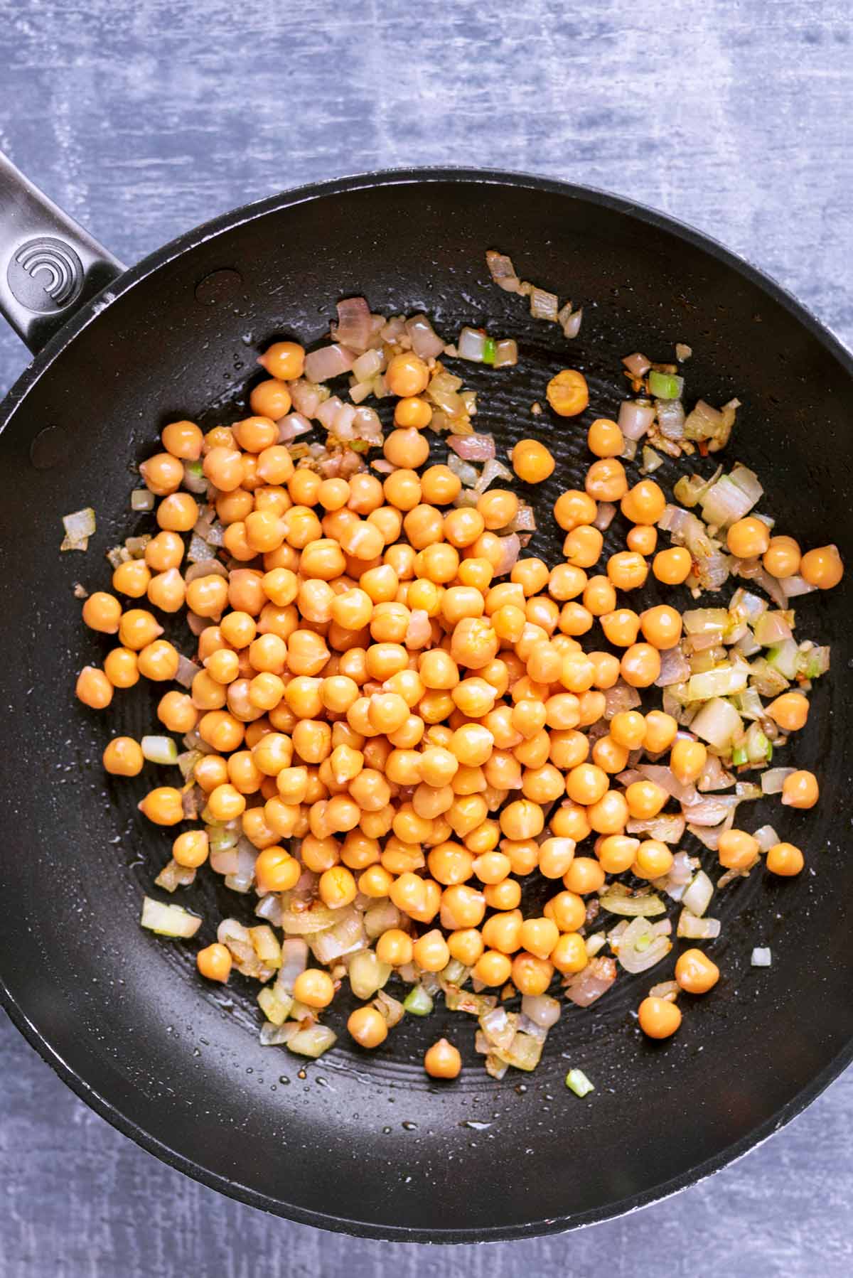 Onions and chickpeas cooking in a frying pan.