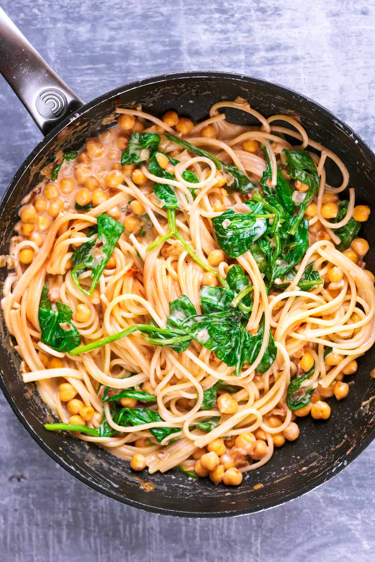 Cooked spaghetti, spinach and chickpeas cooking in a frying pan,