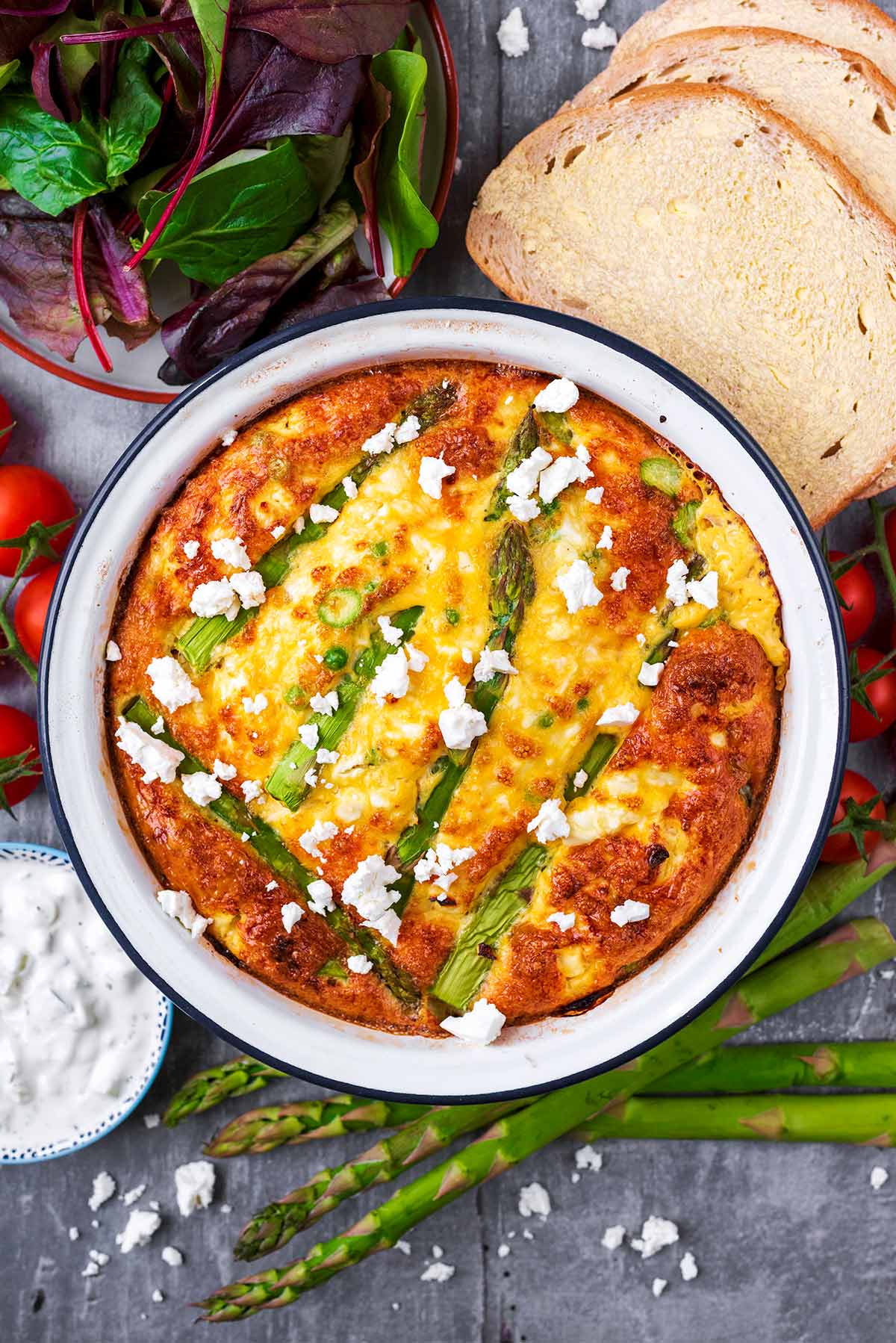 Feta and Asparagus Frittata in a dish next to some asparagus spears and buttered bread.