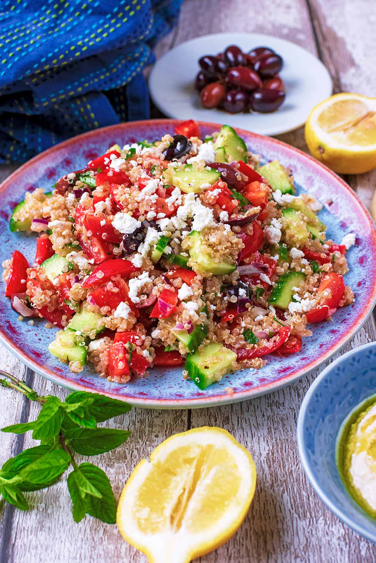 A plate of Quinoa Greek Salad with a half lemon sat in front of it.