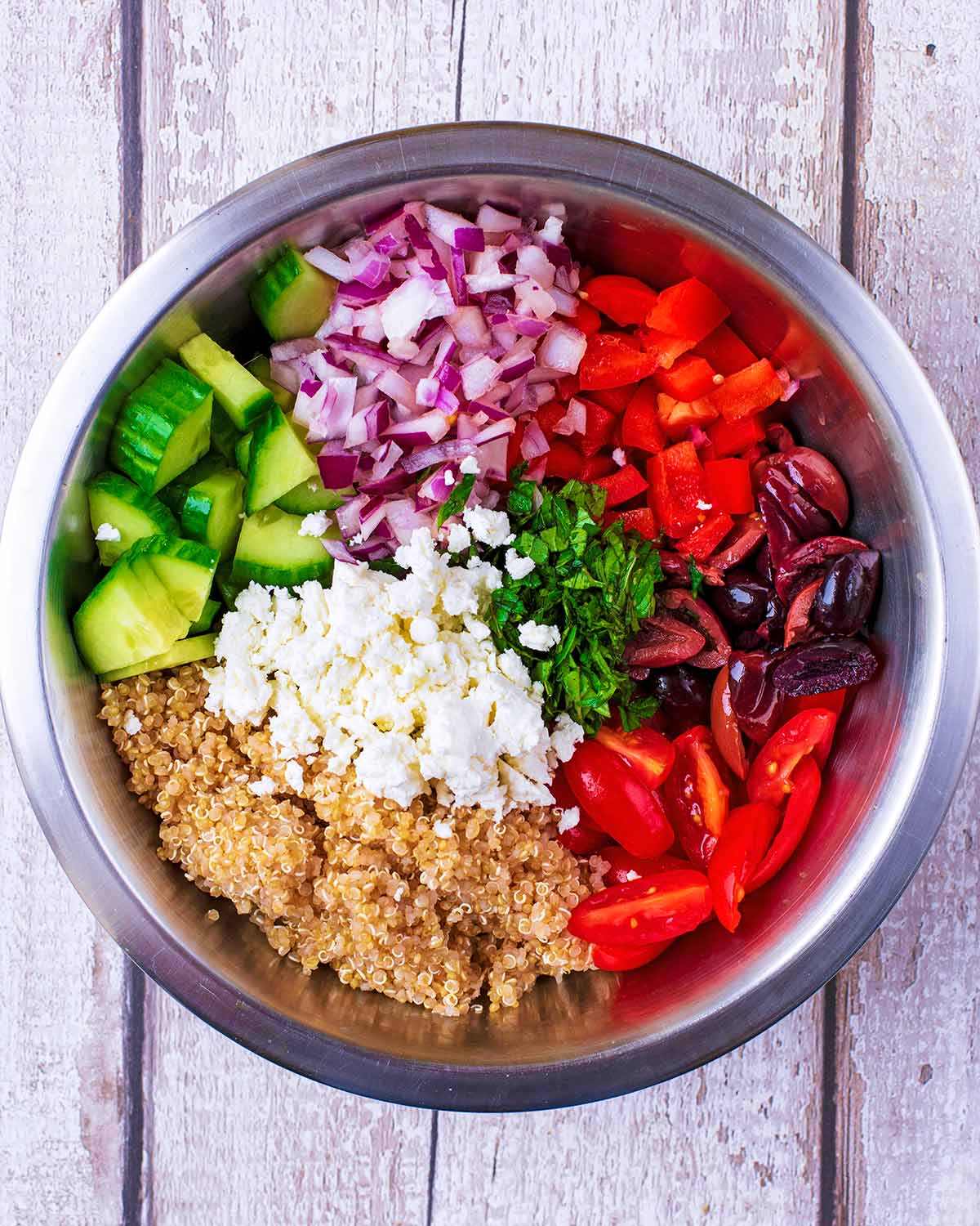 A mixing bowl containing chopped salad, cooked quinoa and a salad dressing.
