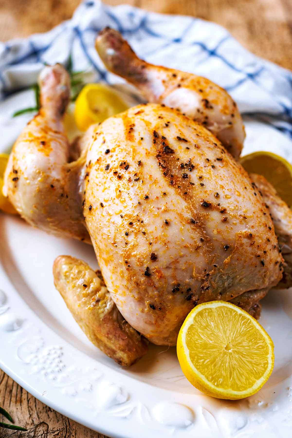 A cooked whole chicken on a plate next to a checked towel.