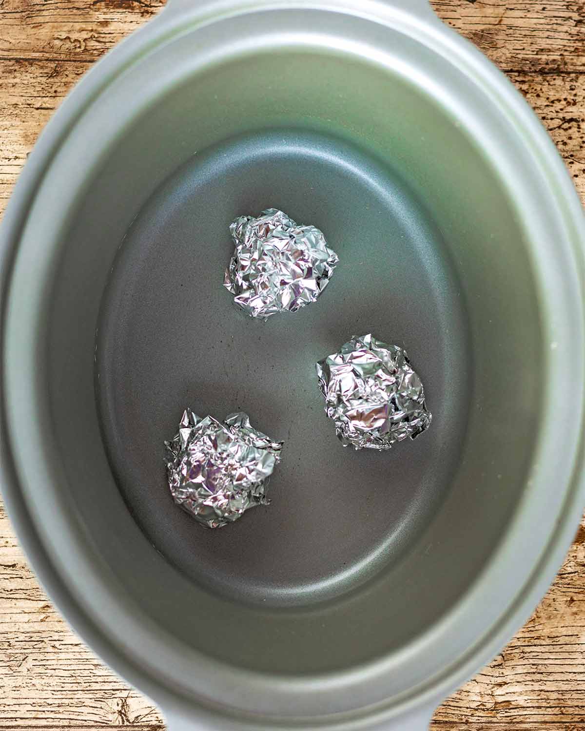 A slow cooker pot with three balls of aluminium foil in the bottom.