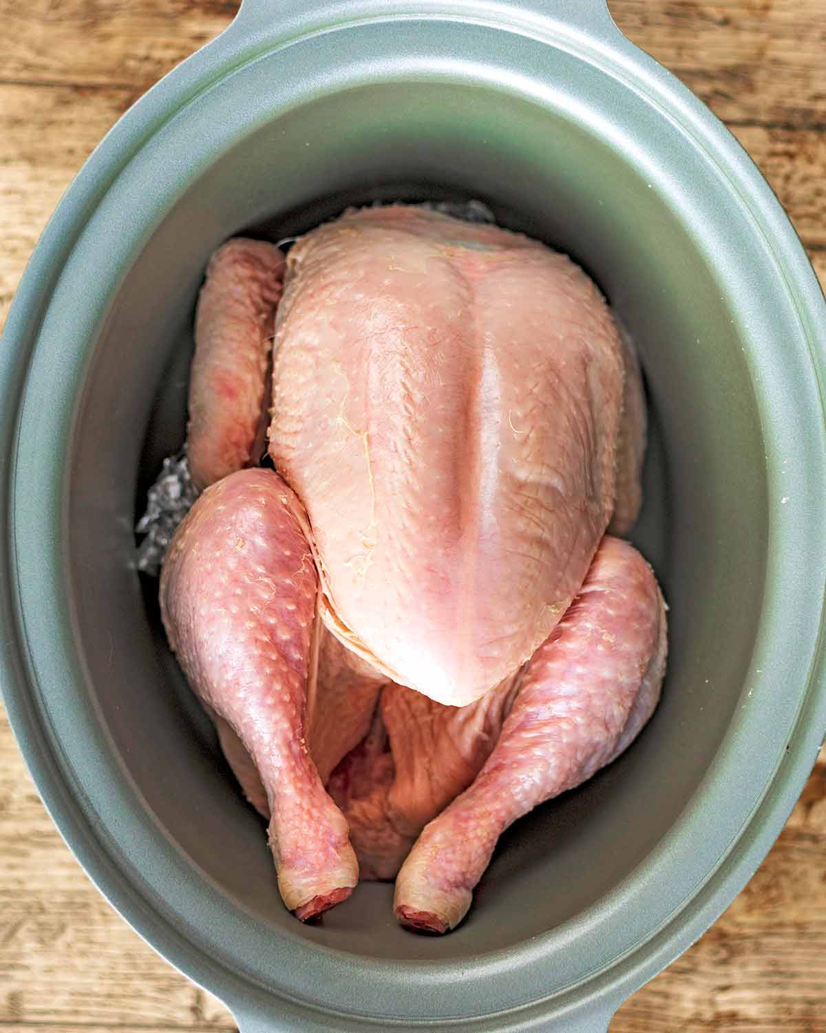 A slow cooker pot with a whole chicken in it.