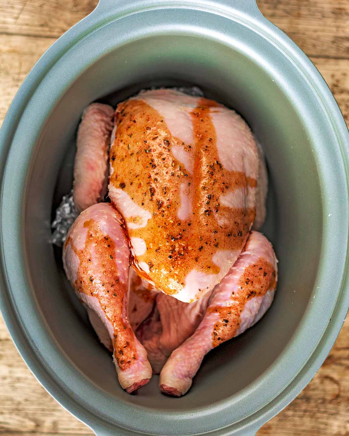 A slow cooker pot with a whole chicken covered in a sauce.