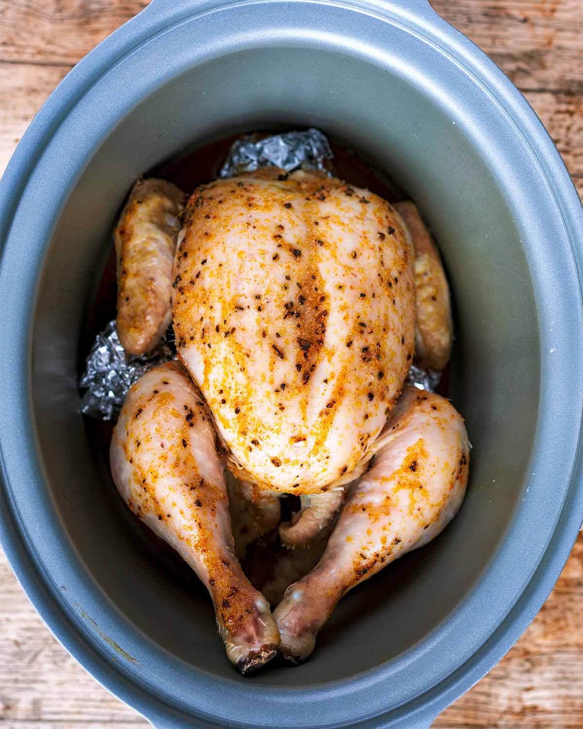 A cooked whole chicken in a slow cooker pot.