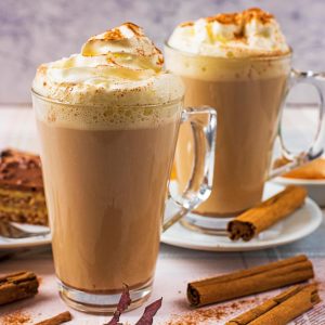 Cinnamon Coffee in two lattes in glasses with cinnamon sticks and a slice of cake