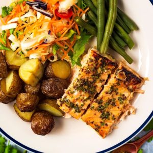 Honey Mustard Salmon on a plate with potatoes, beans and slaw